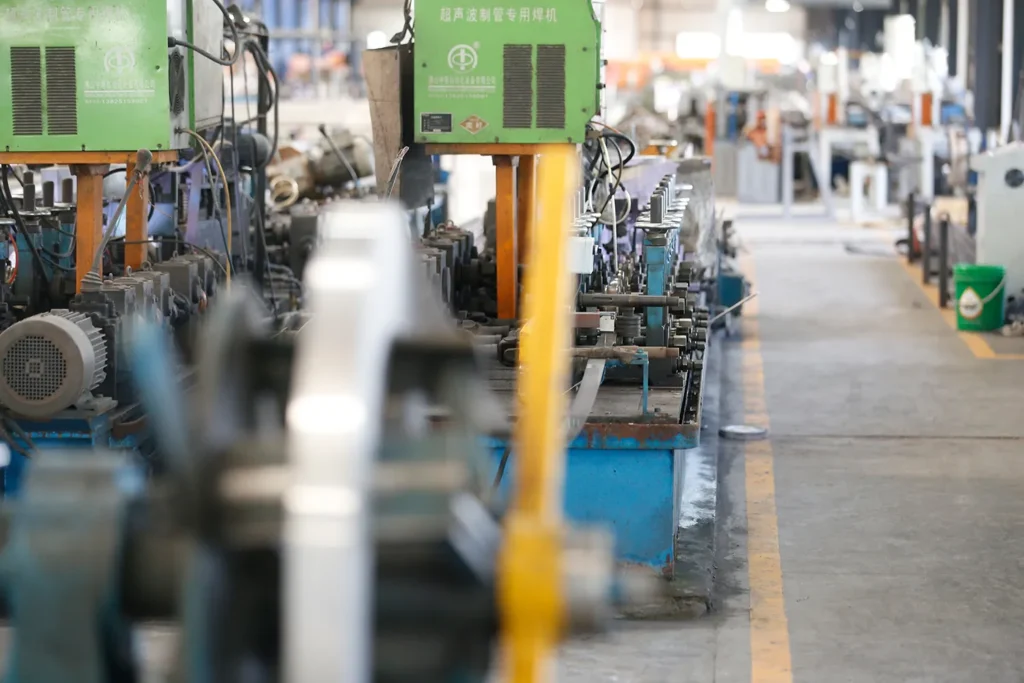 Multiple automated tube mill machines actively producing stainless steel pipes in clean, well-maintained factory environment with proper lighting and space.