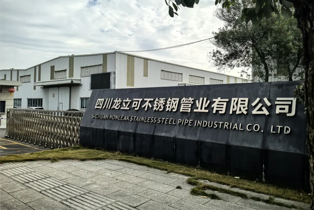 Main entrance and facade of Longlike Nonleak Stainless Steel Pipe Industry Co., Ltd. in Guanghan, showing the company sign in both Chinese and English with modern factory buildings in the background.