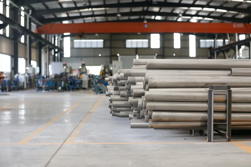 Clean and organized manufacturing workshop showing finished stainless steel pipes neatly stacked in foreground with rows of tube mill machines in background at Nonleak facility.